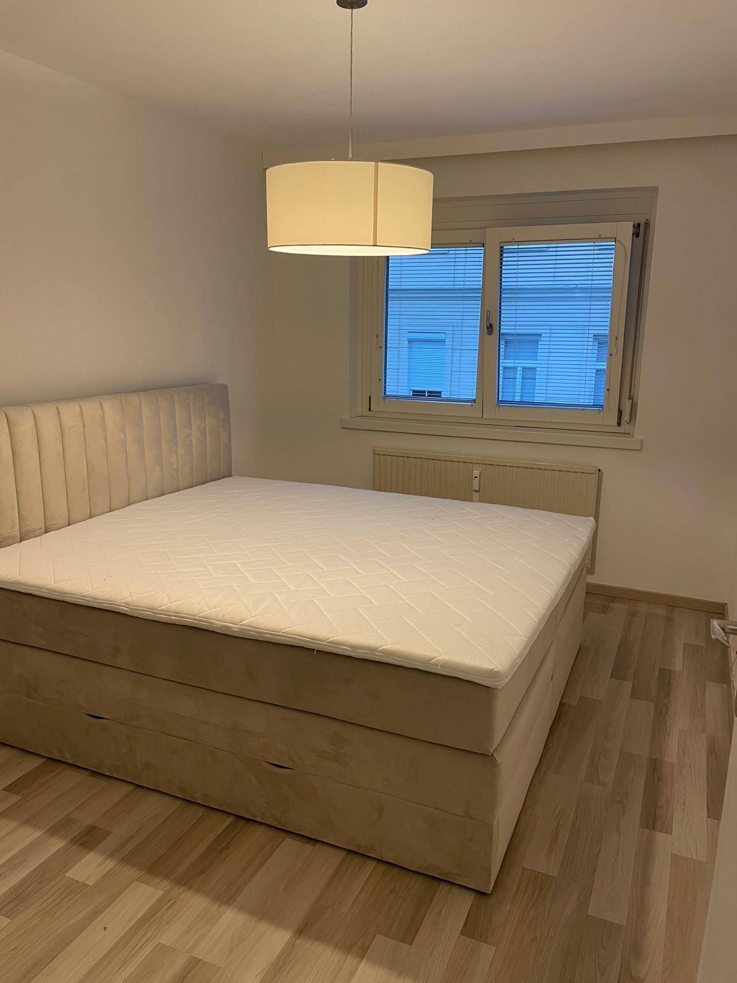 Gemütliches Schlafzimmer mit großem Bett, hellem Laminatboden und Fenster für Tageslicht.