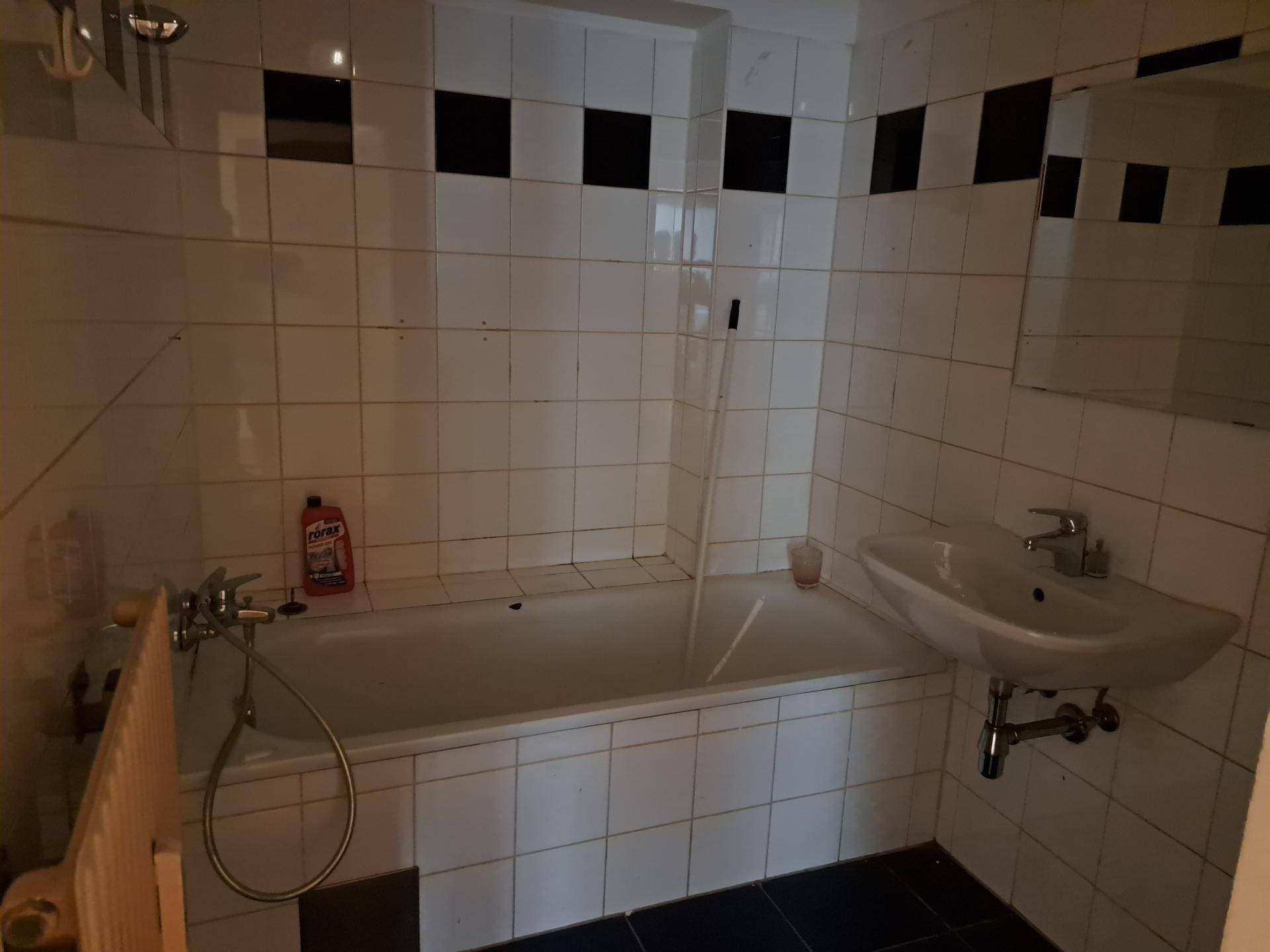 Badezimmer mit Badewanne, Waschbecken und weiß-schwarzen Fliesen in einfachem Design.