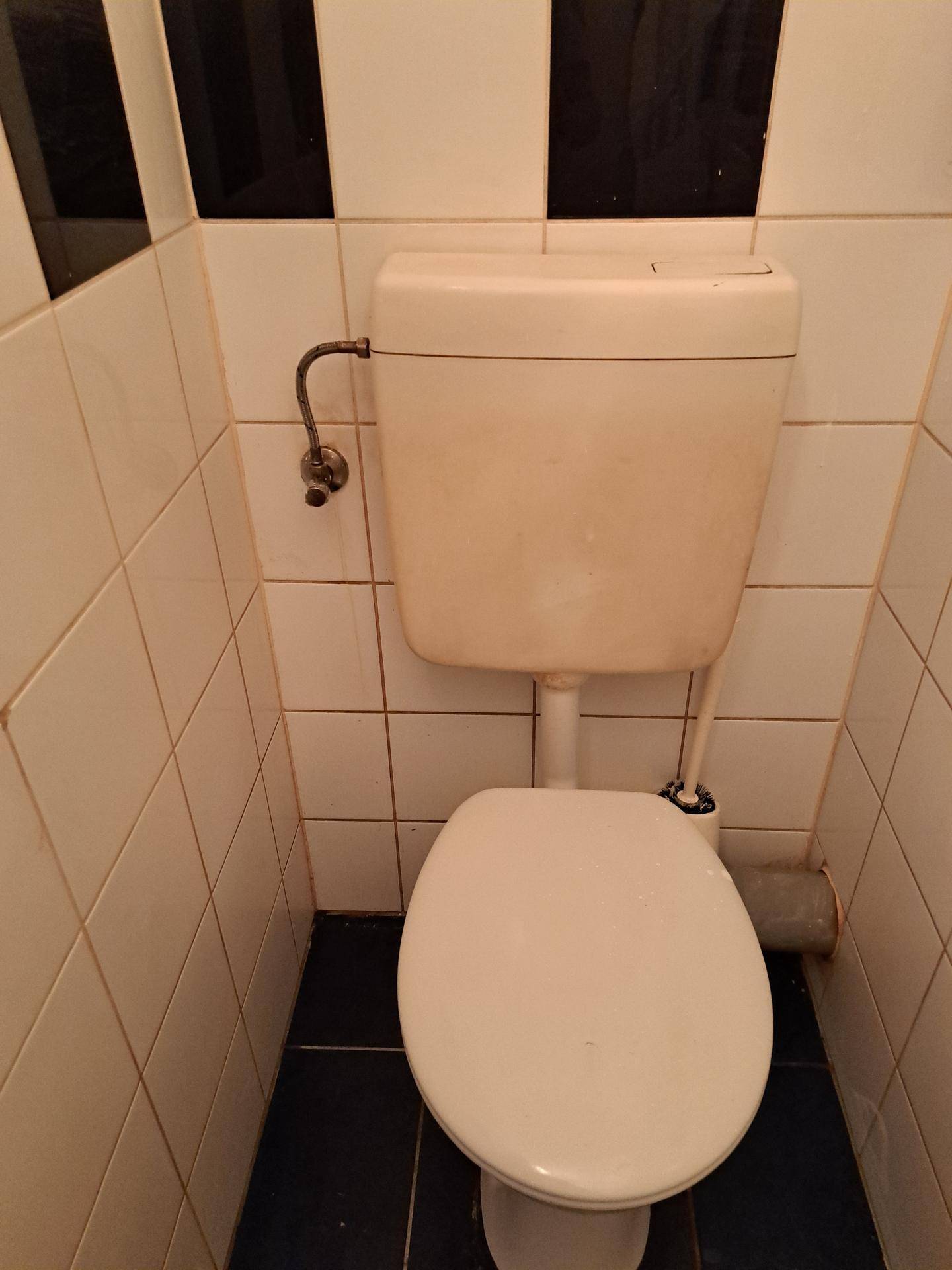 Kleines WC mit weiß-schwarzen Fliesen und einfacher Toilette in funktionalem Zustand.