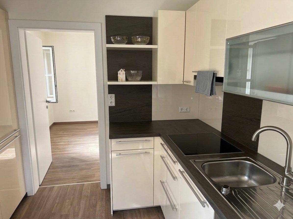 Moderne Einbauküche mit hellen Schränken, dunkler Arbeitsplatte und Induktionskochfeld.