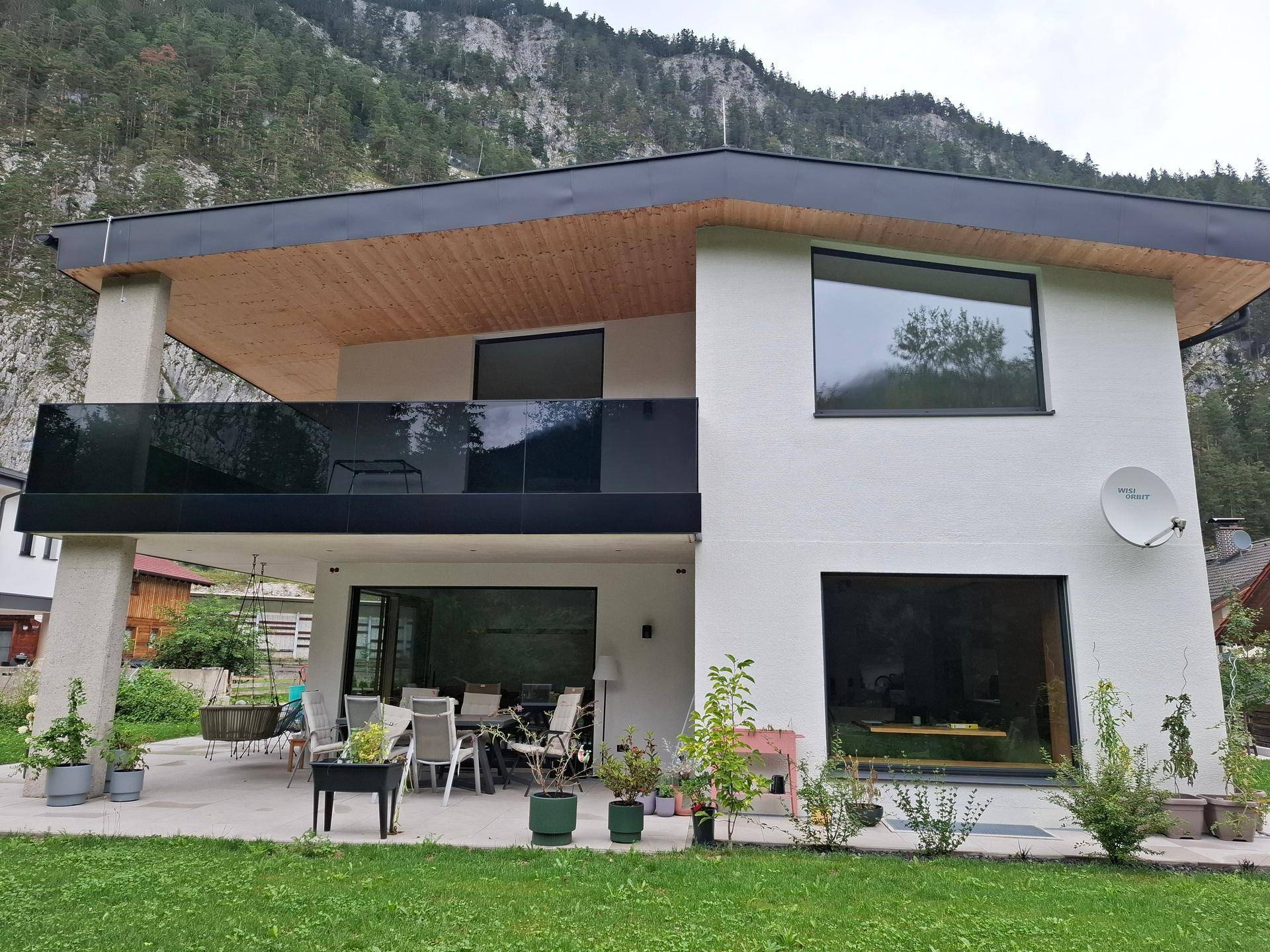Rückansicht des modernen Hauses mit großen Fenstern, Terrasse und Bergblick.