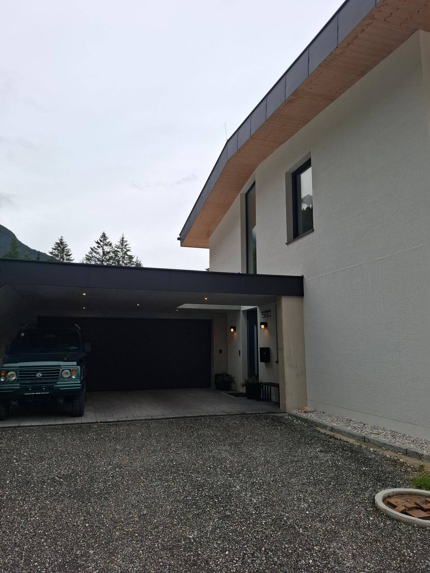 Seitenansicht des modernen Hauses mit integriertem Carport und Zufahrt.
