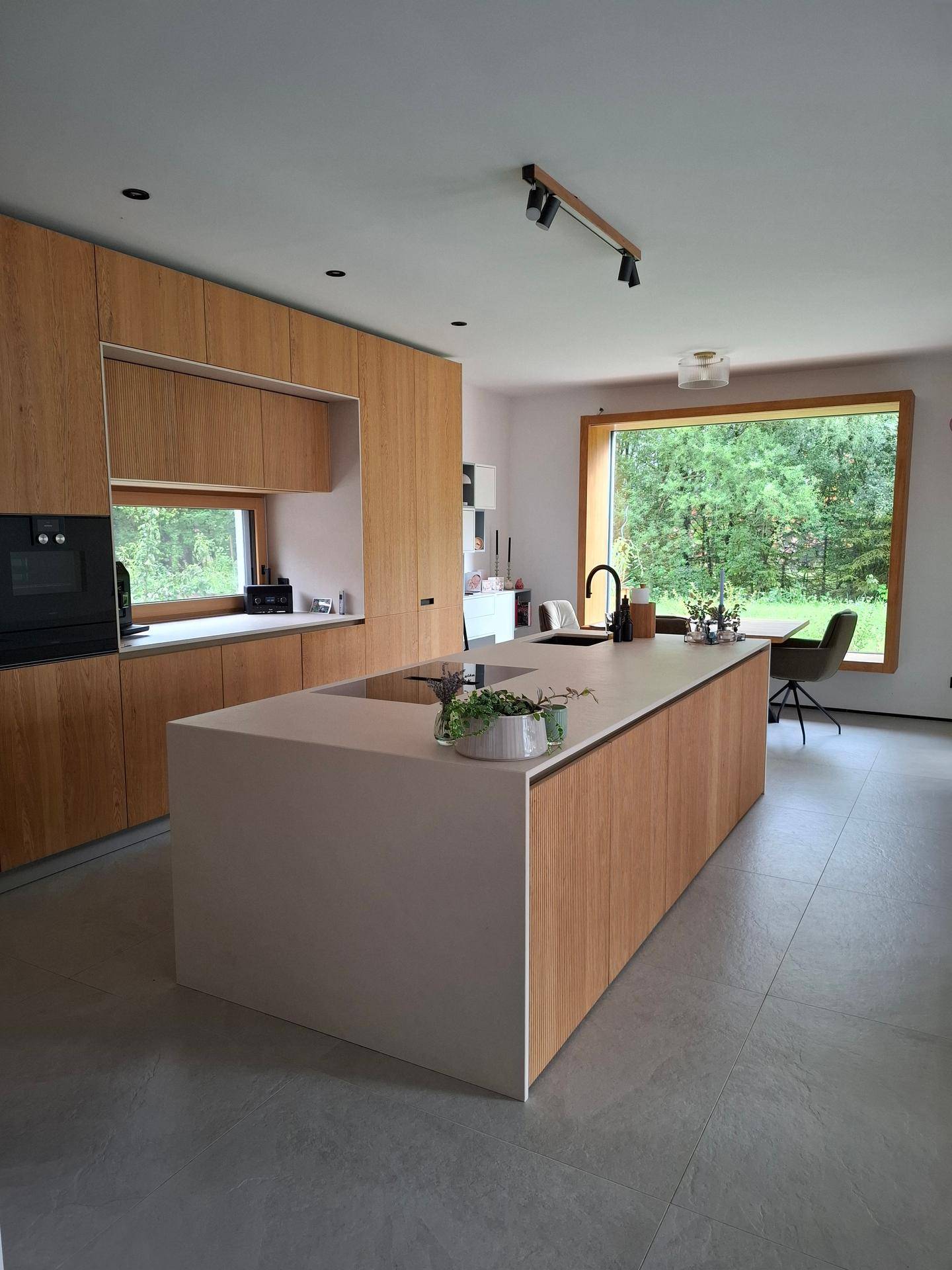 Moderne Küche mit Holzfronten, Kücheninsel und Essbereich mit Blick ins Grüne.