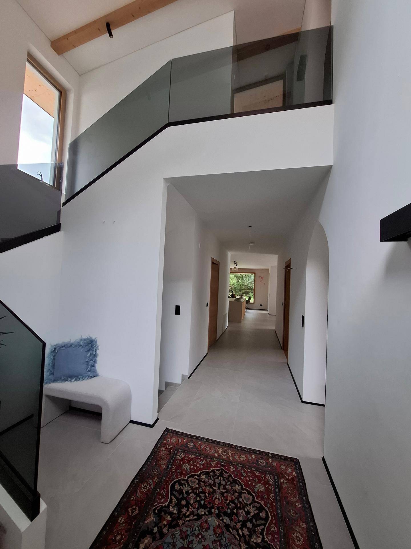 Geräumiger Flur mit moderner Glasbrüstung, Sitzbank und Blick in den Wohnbereich.