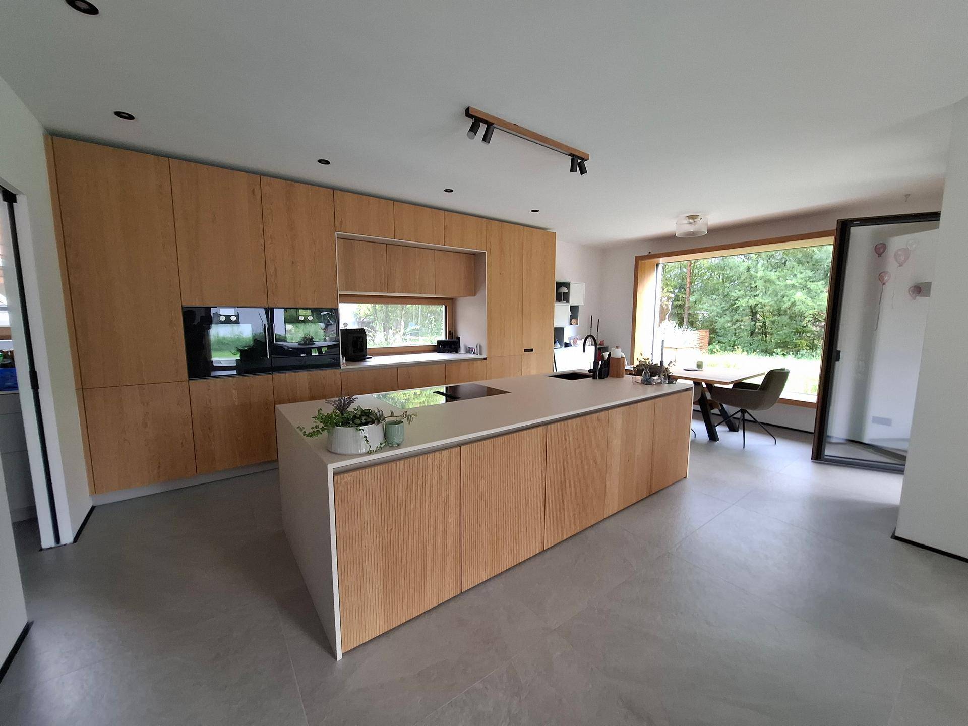 Moderne Küche mit Holzfronten, Kücheninsel und Essbereich mit Blick ins Grüne.