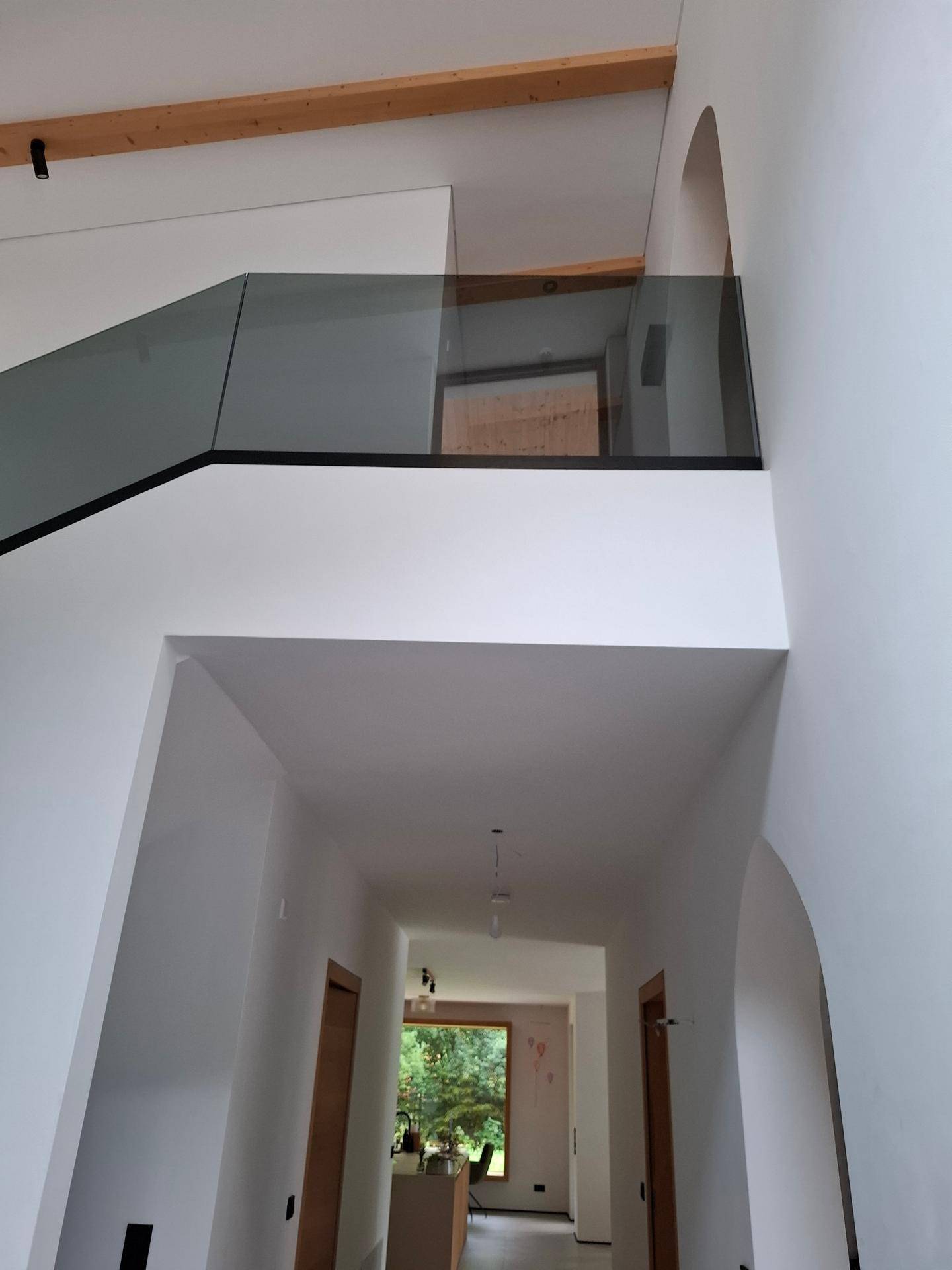Heller Flur mit moderner Glasbrüstung, Holzdeckenbalken und Blick in den unteren Bereich.