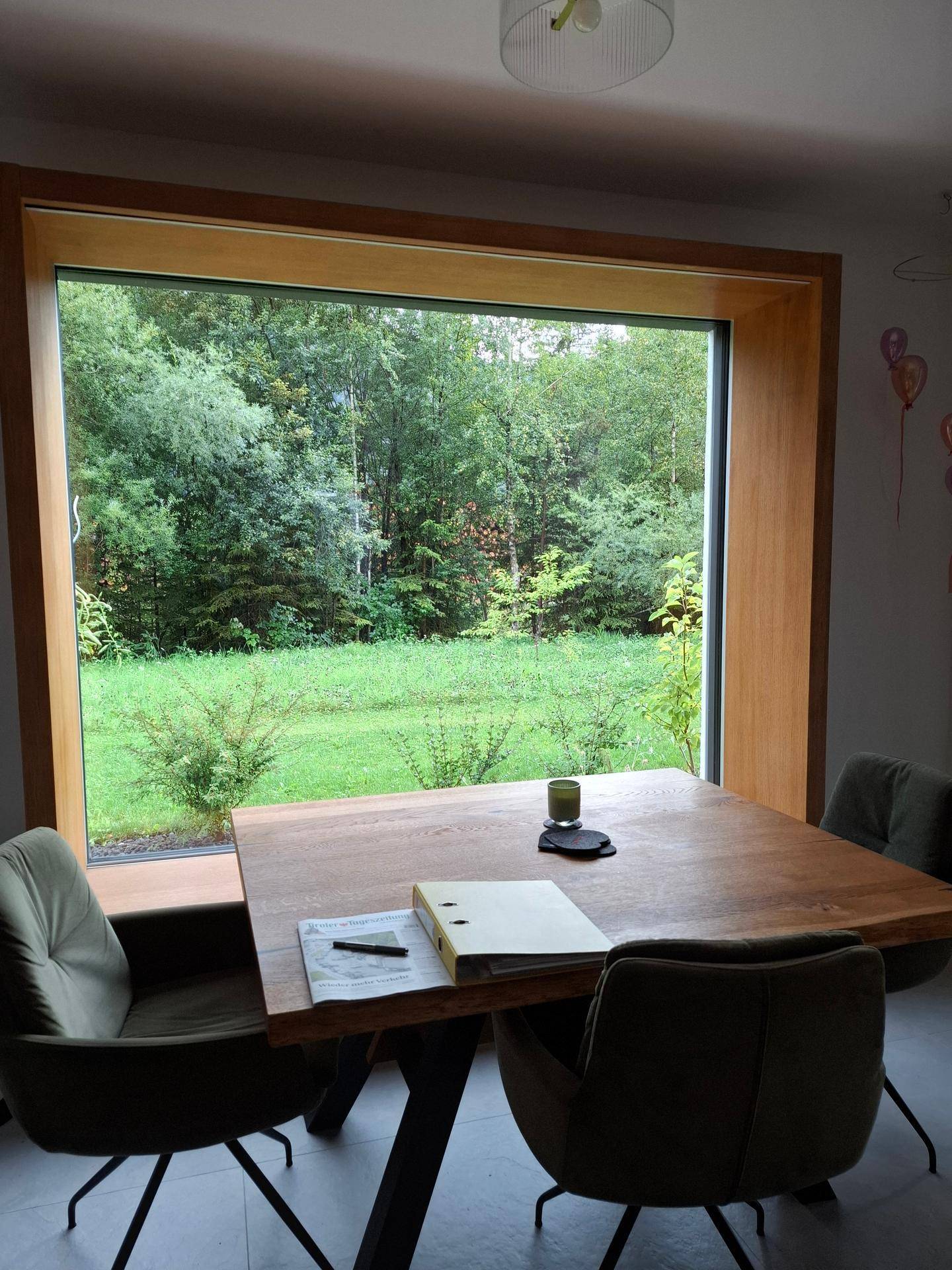 Essbereich mit Holztisch und großem Fenster, das einen schönen Blick ins Grüne bietet.