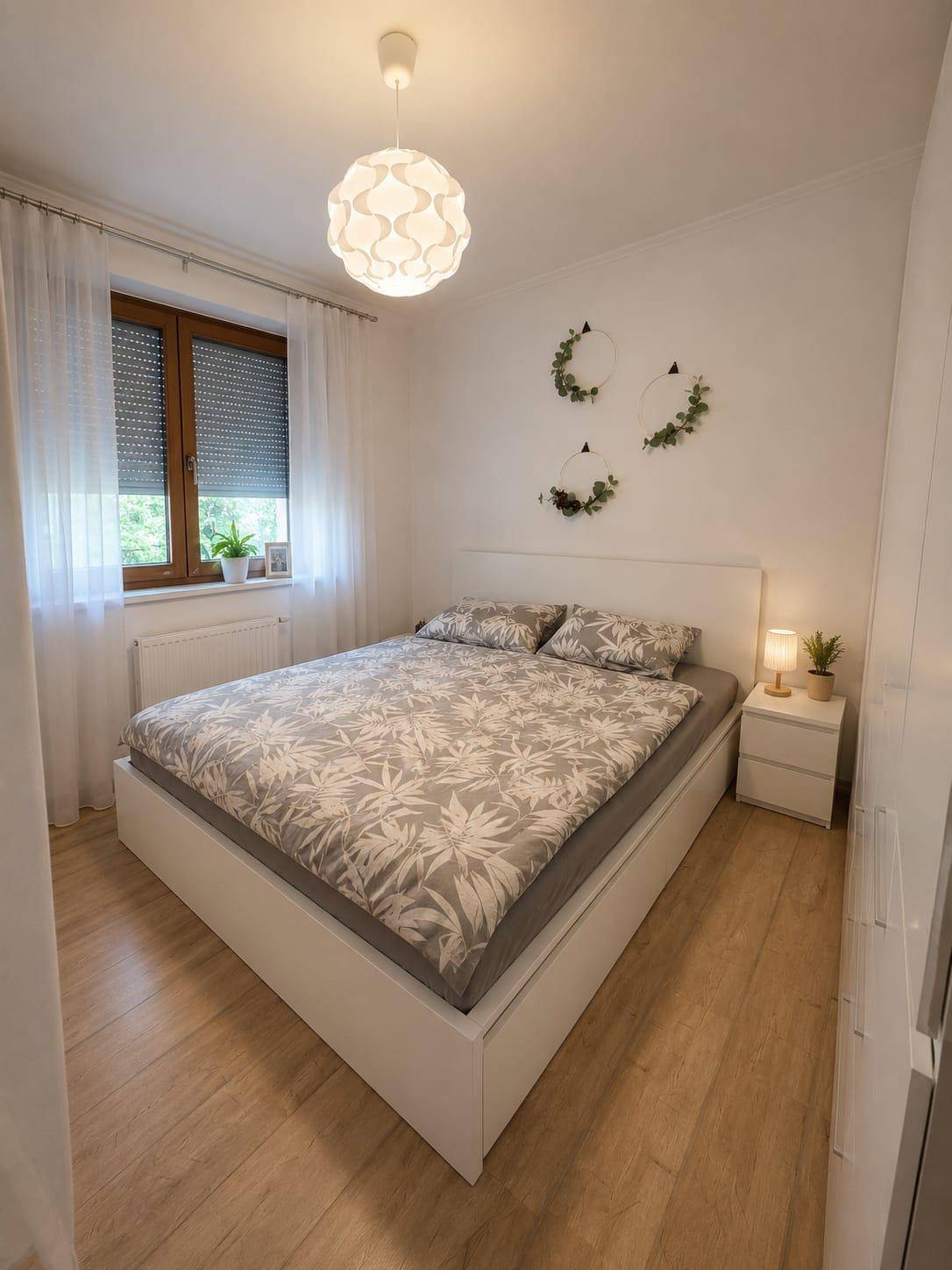 Ruhiges Schlafzimmer mit Doppelbett, hellem Laminatboden und Fensterblick ins Grüne.