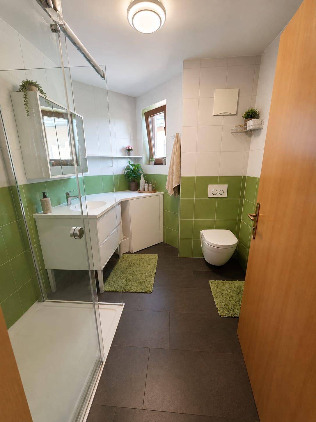 Modernes Badezimmer mit Dusche, grünen Fliesen und Fenster für Tageslicht.