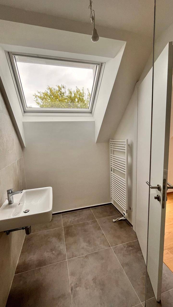 Modernes Badezimmer mit Waschbecken, Dachfenster und beheiztem Handtuchhalter in hellen Tönen.