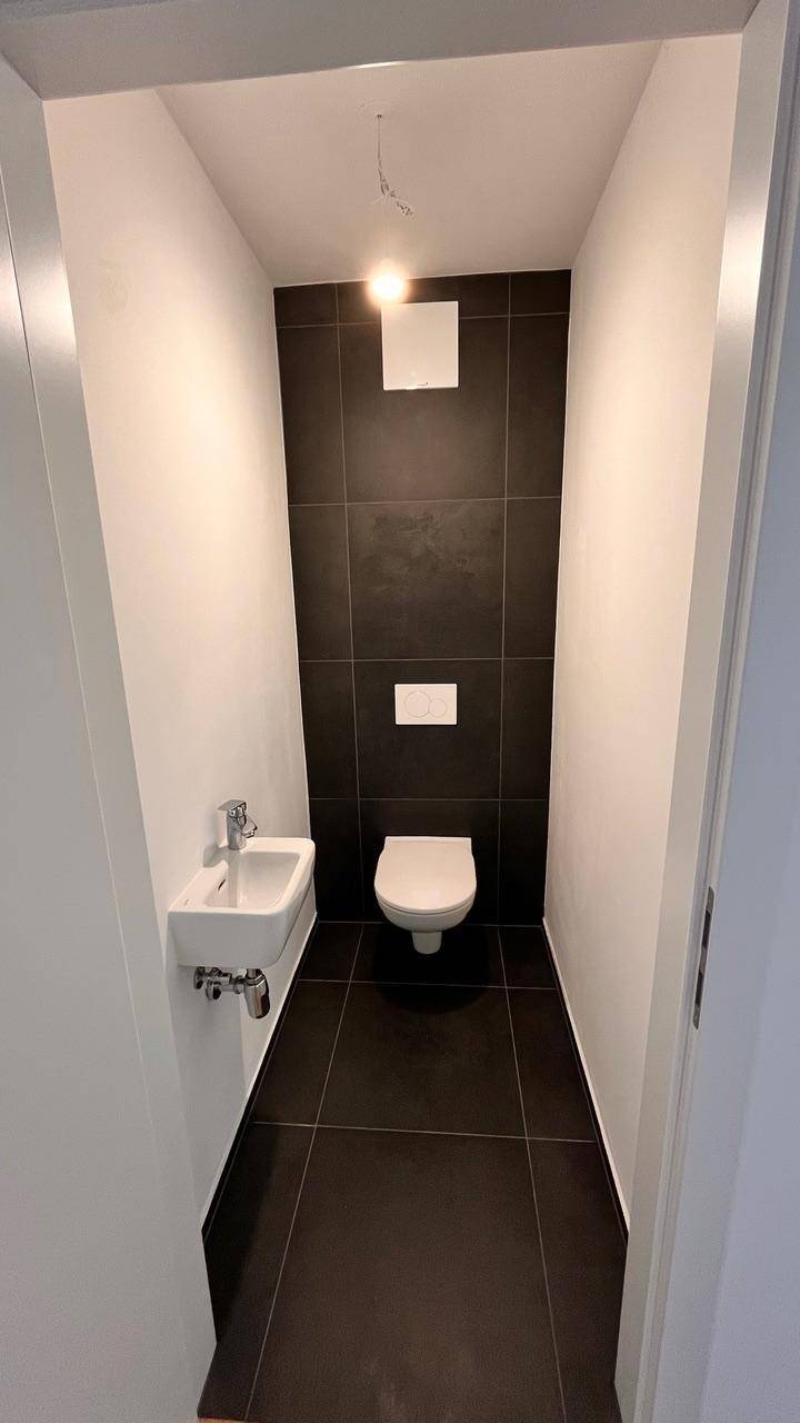 Modernes Gäste-WC mit dunklen Fliesen, wandhängendem WC und kleinem Waschbecken.