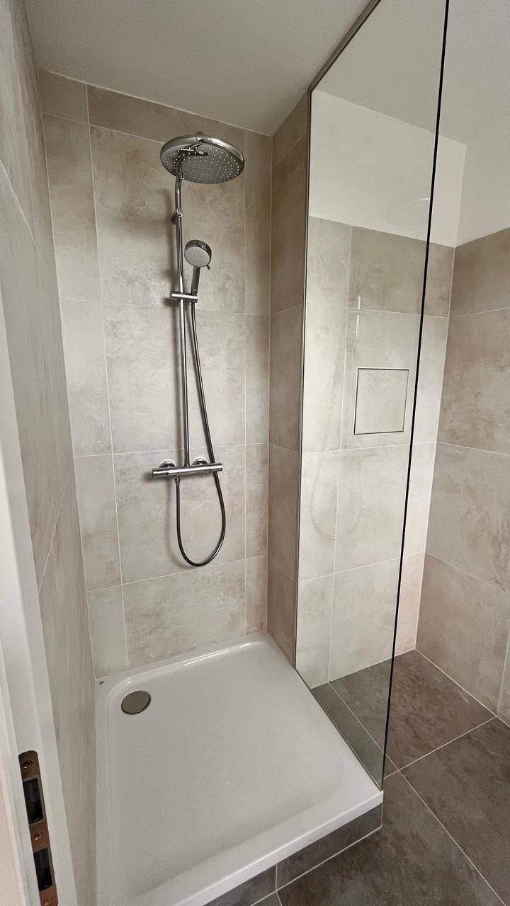Moderne Duschkabine mit Glaswand und beigefarbenen Fliesen im Badezimmer.