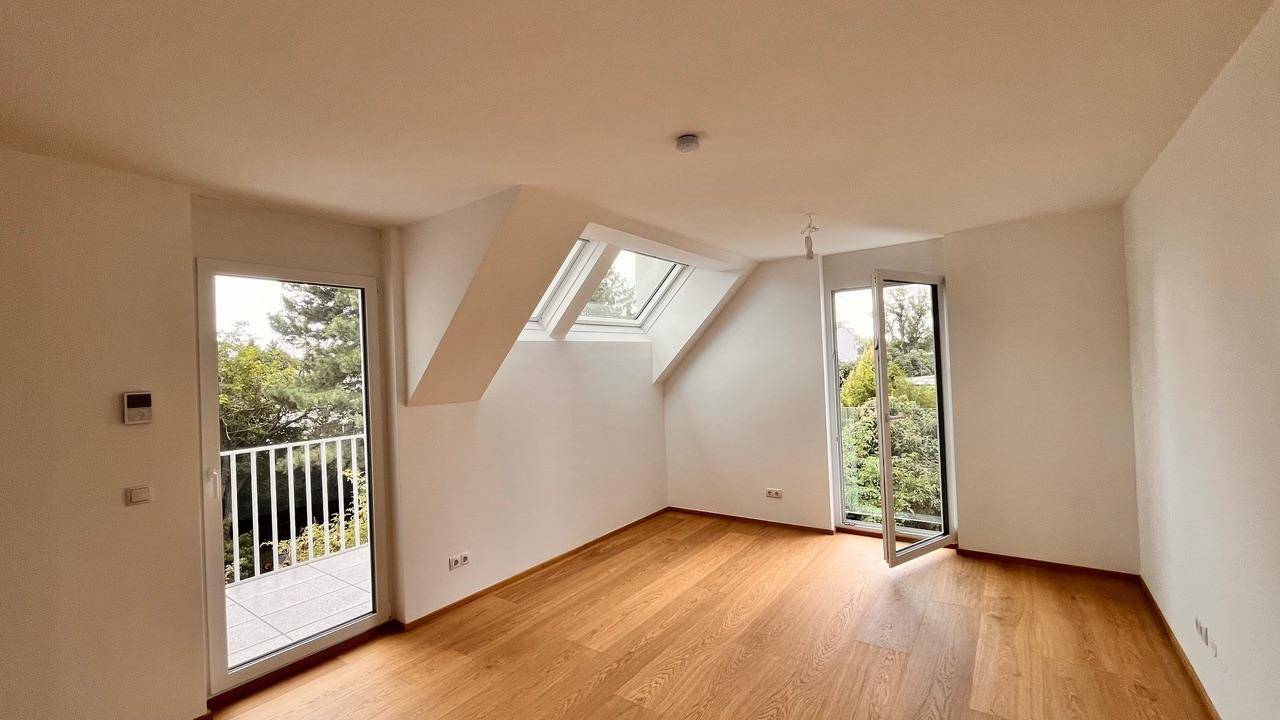 Heller Wohnraum mit Holzboden, Dachschrägen, Dachfenstern und Zugang zu einem Balkon.
