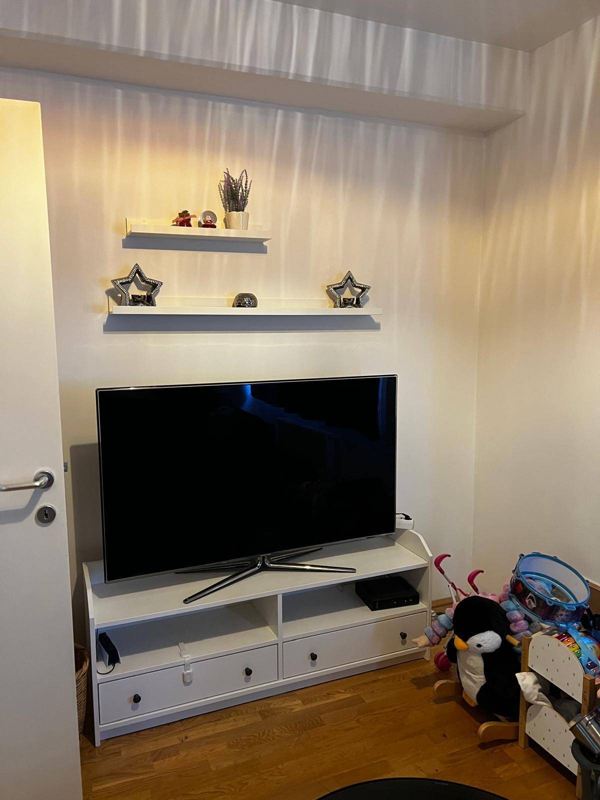 Wohnbereich mit großem Fernseher auf einem Lowboard und dekorativen Wandregalen.