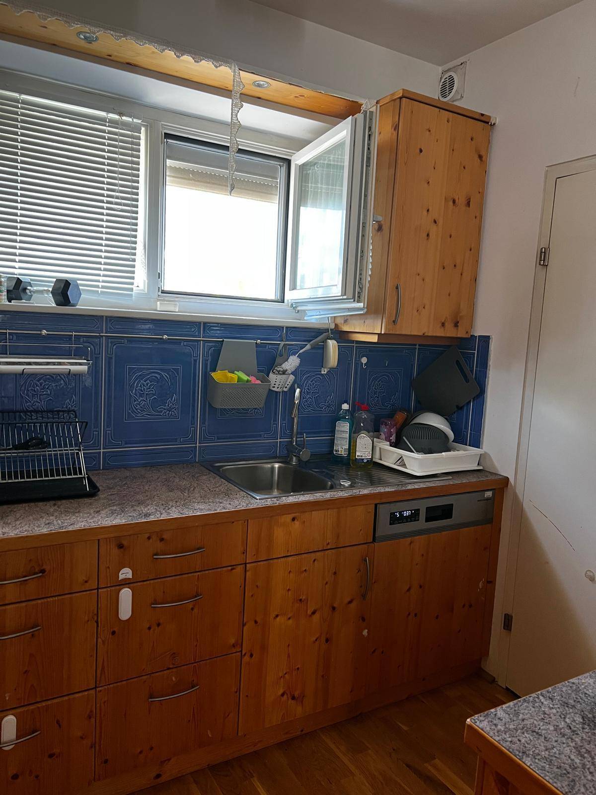 Küchenspüle mit Holzunterschränken, blauer Fliesenrückwand und einem Fenster für natürliches Licht.