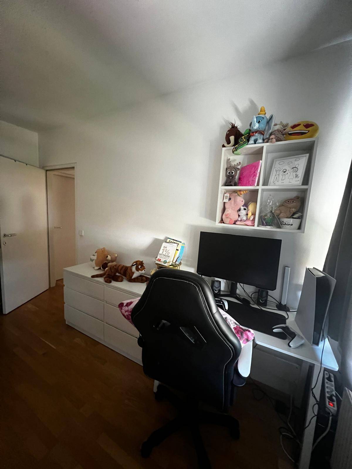 Arbeitsbereich mit Schreibtisch, Computer und Regalen für Dekorationen und persönliche Gegenstände.