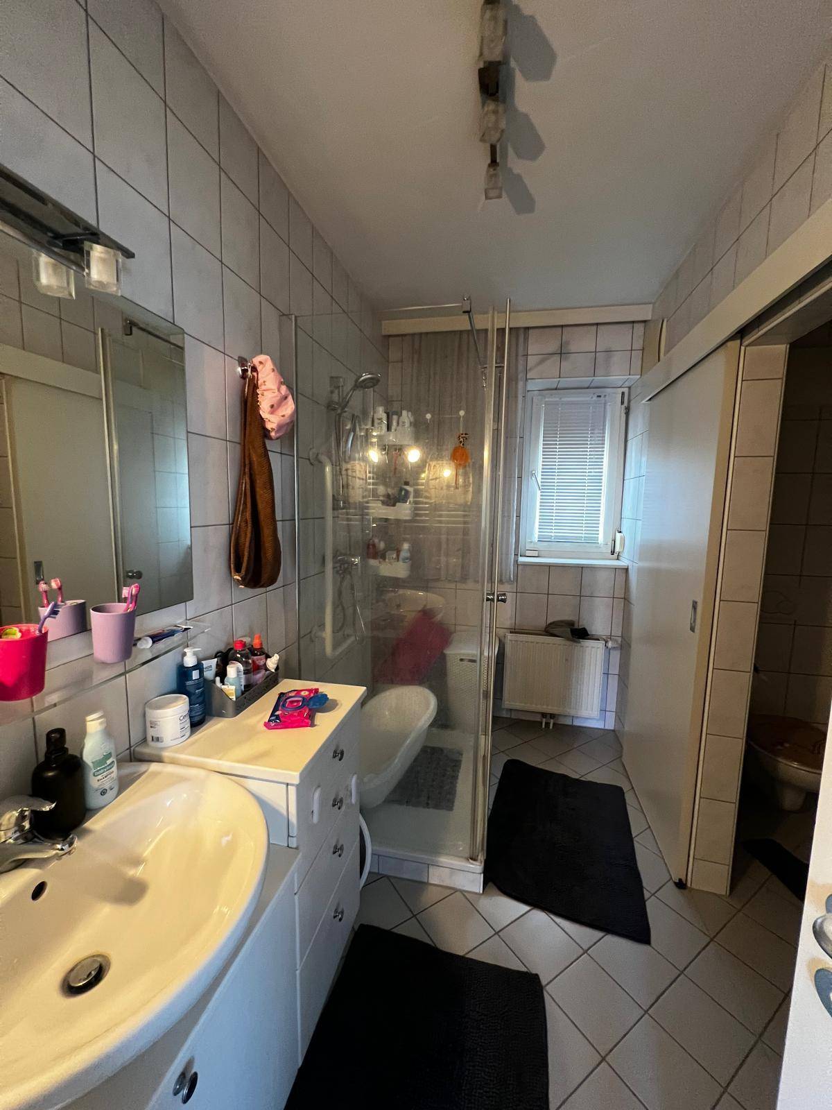 Badezimmer mit Duschkabine, Waschbecken und einer separaten Toilette hinter einer Schiebetür.