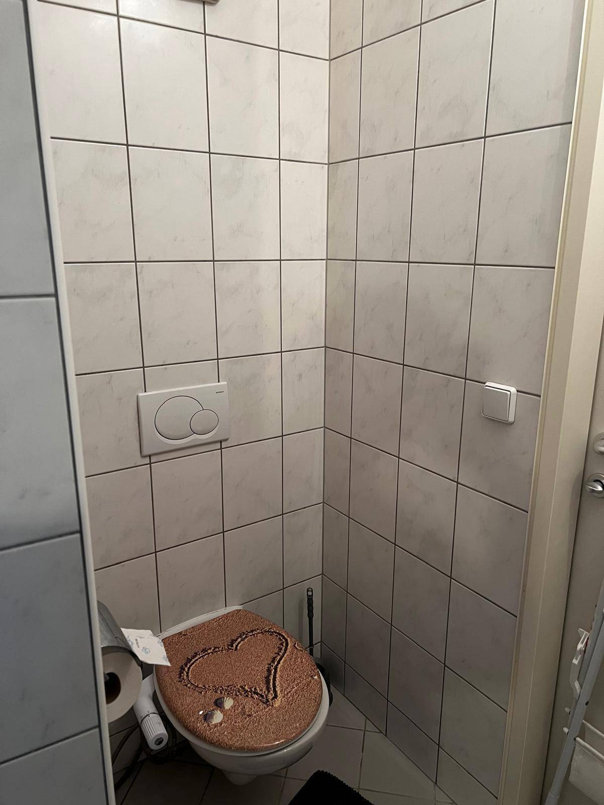 Separate Toilette mit hellen Fliesen an Wänden und Boden, ausgestattet mit Wand-WC.