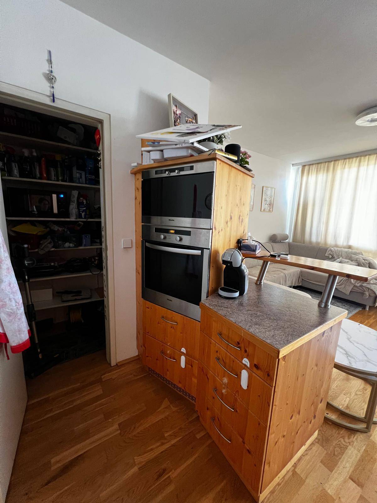 Eingebauter Backofen und Mikrowelle in einem Holzschrank, neben einer praktischen Speisekammer.