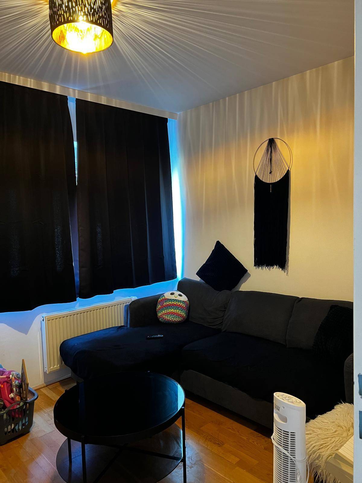 Gemütliches Wohnzimmer mit dunklem Ecksofa, Couchtisch und blickdichten Vorhängen.