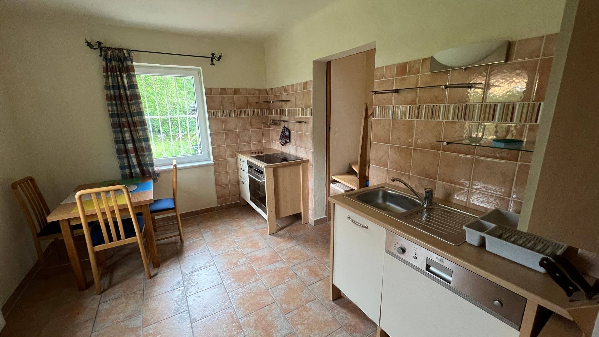 Funktionale Küche mit Essbereich, Fliesenboden und Fenster zum Garten.