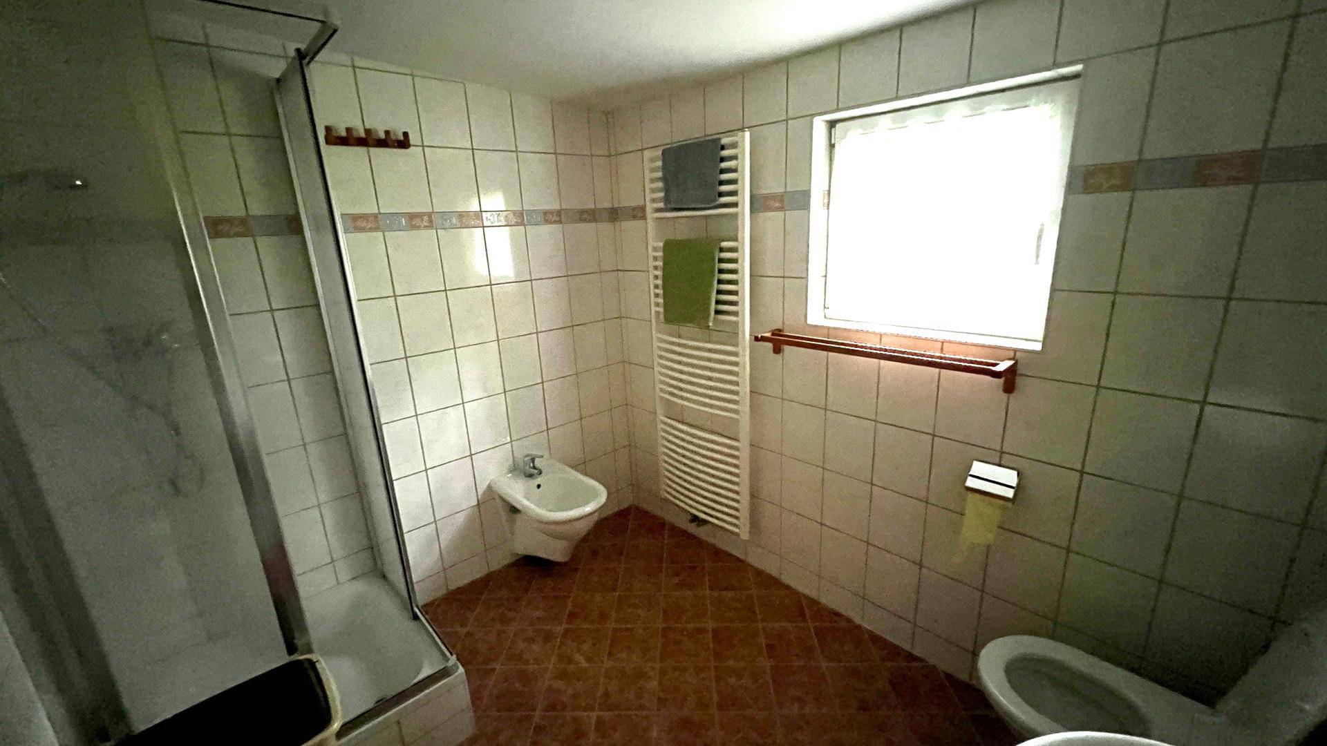 Gefliestes Badezimmer mit Dusche, Bidet, WC und beheiztem Handtuchhalter.