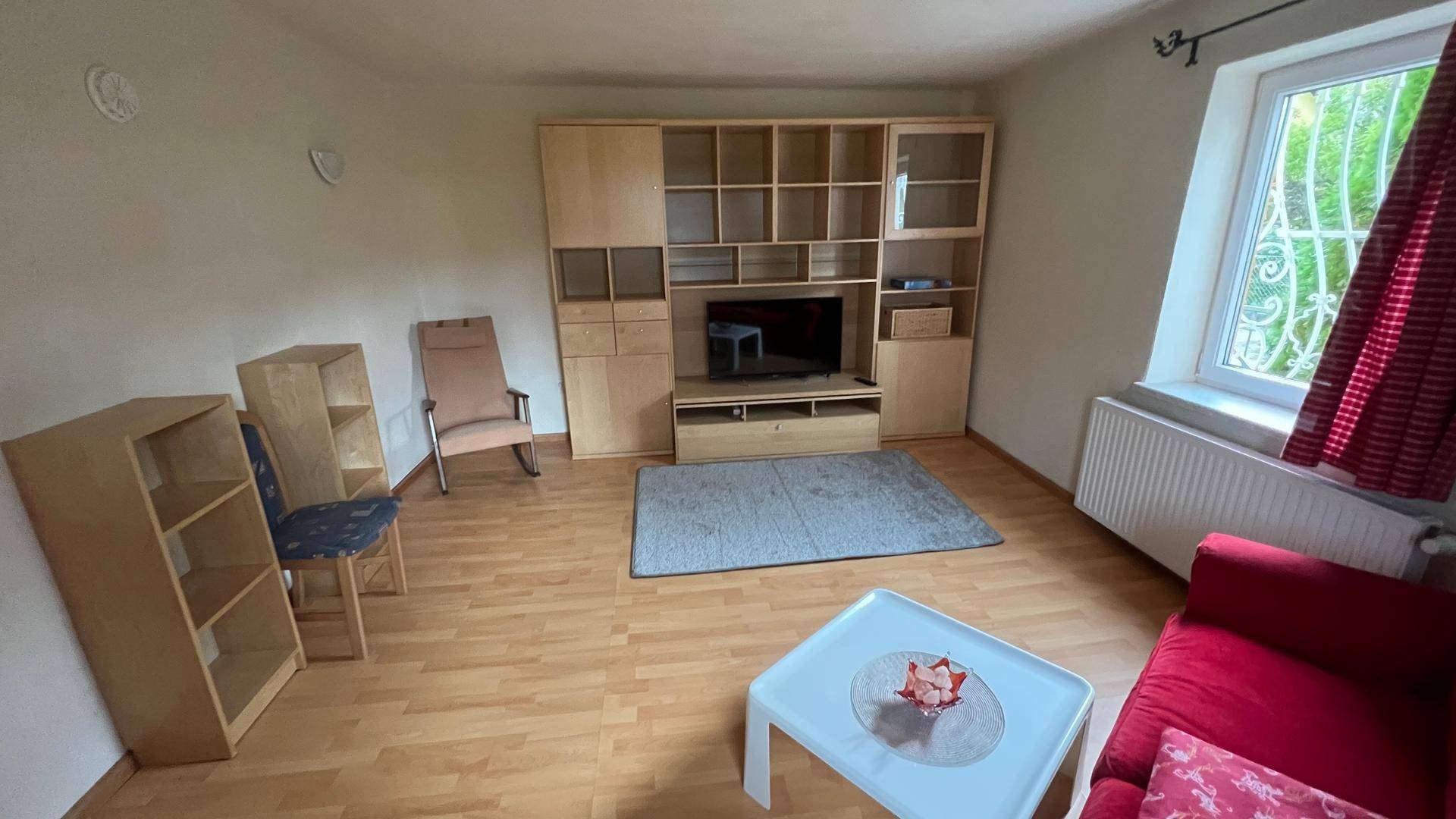 Wohnzimmer mit Holzparkett, großem Fenster und Stauraum durch Regale.