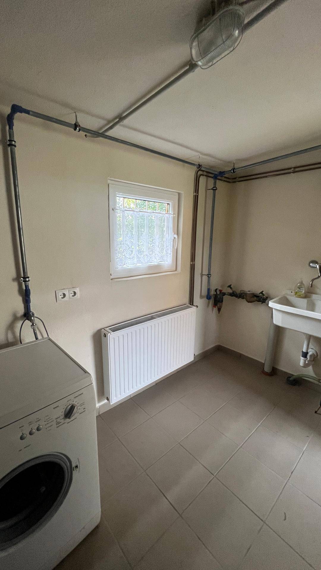 Praktische Waschküche mit Waschmaschine, Spülbecken und pflegeleichtem Fliesenboden.