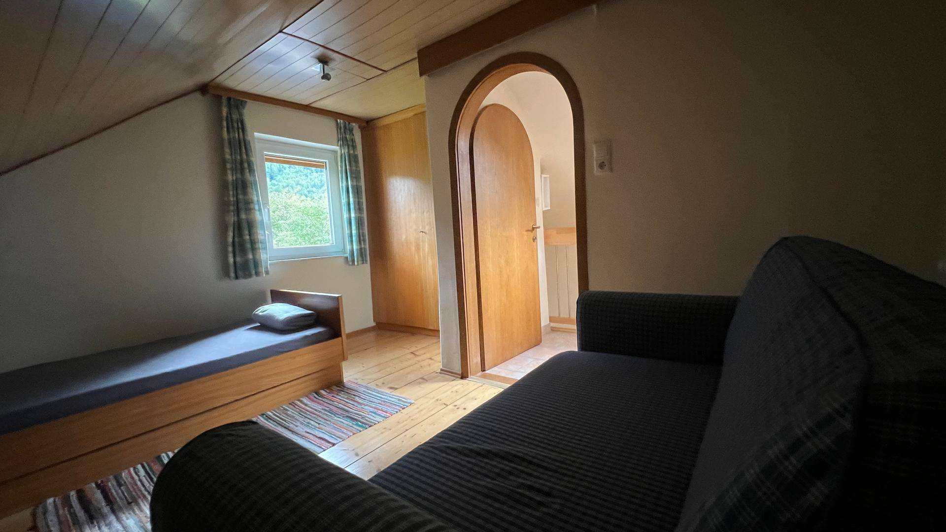 Schlafzimmer im Dachgeschoss mit Einzelbett, Sofa und Holzboden.