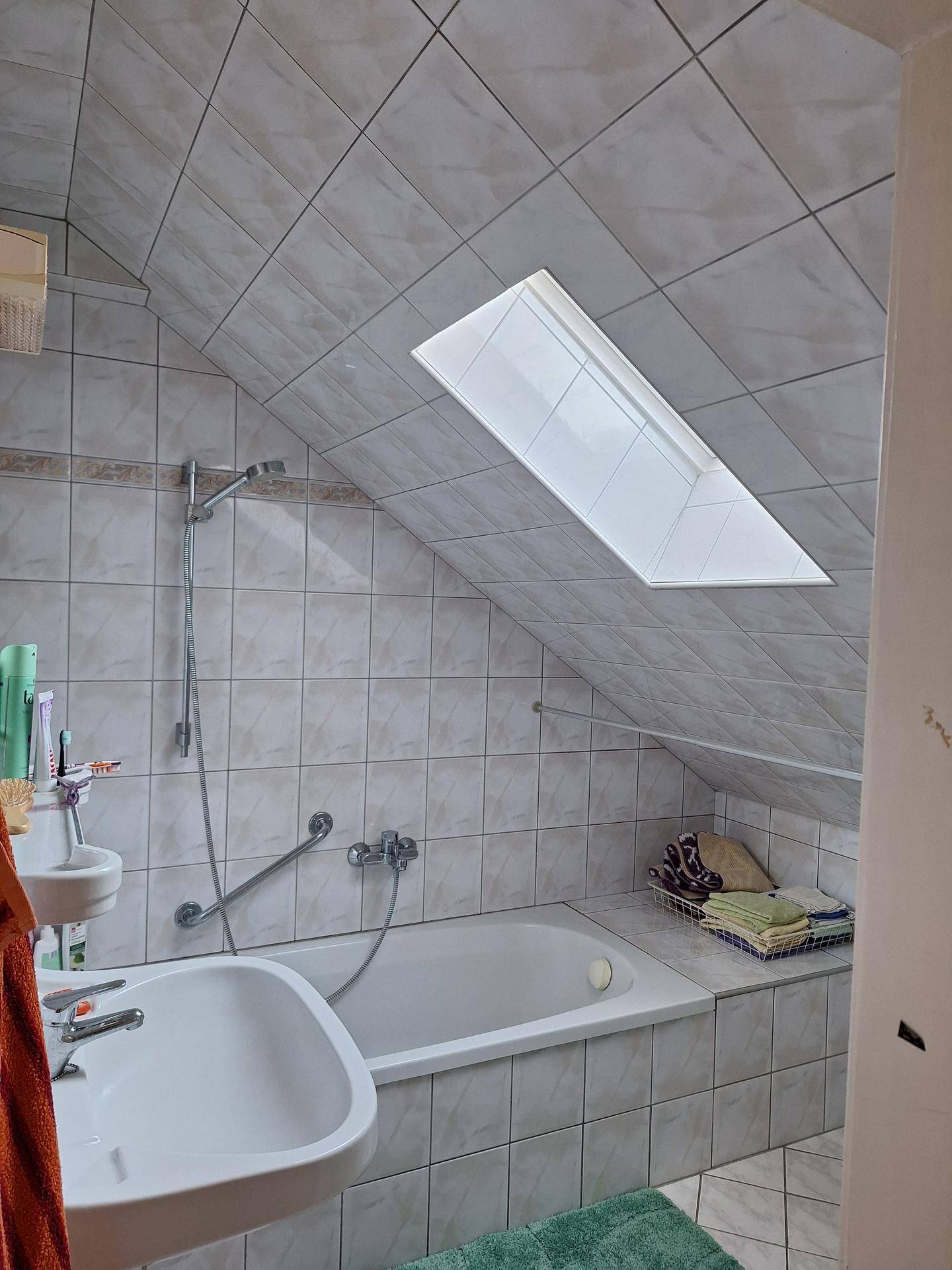 Gefliestes Badezimmer mit Badewanne, Waschbecken und Dachfenster in der Dachschräge.