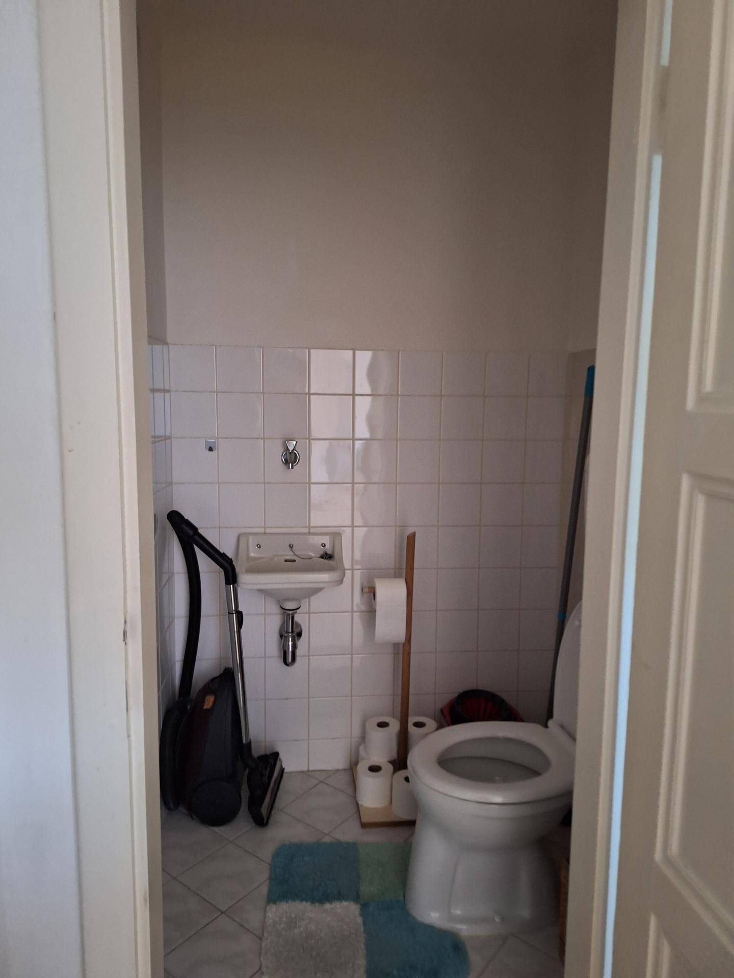 Kleines WC mit Toilette, Handwaschbecken und weißen Wandfliesen.