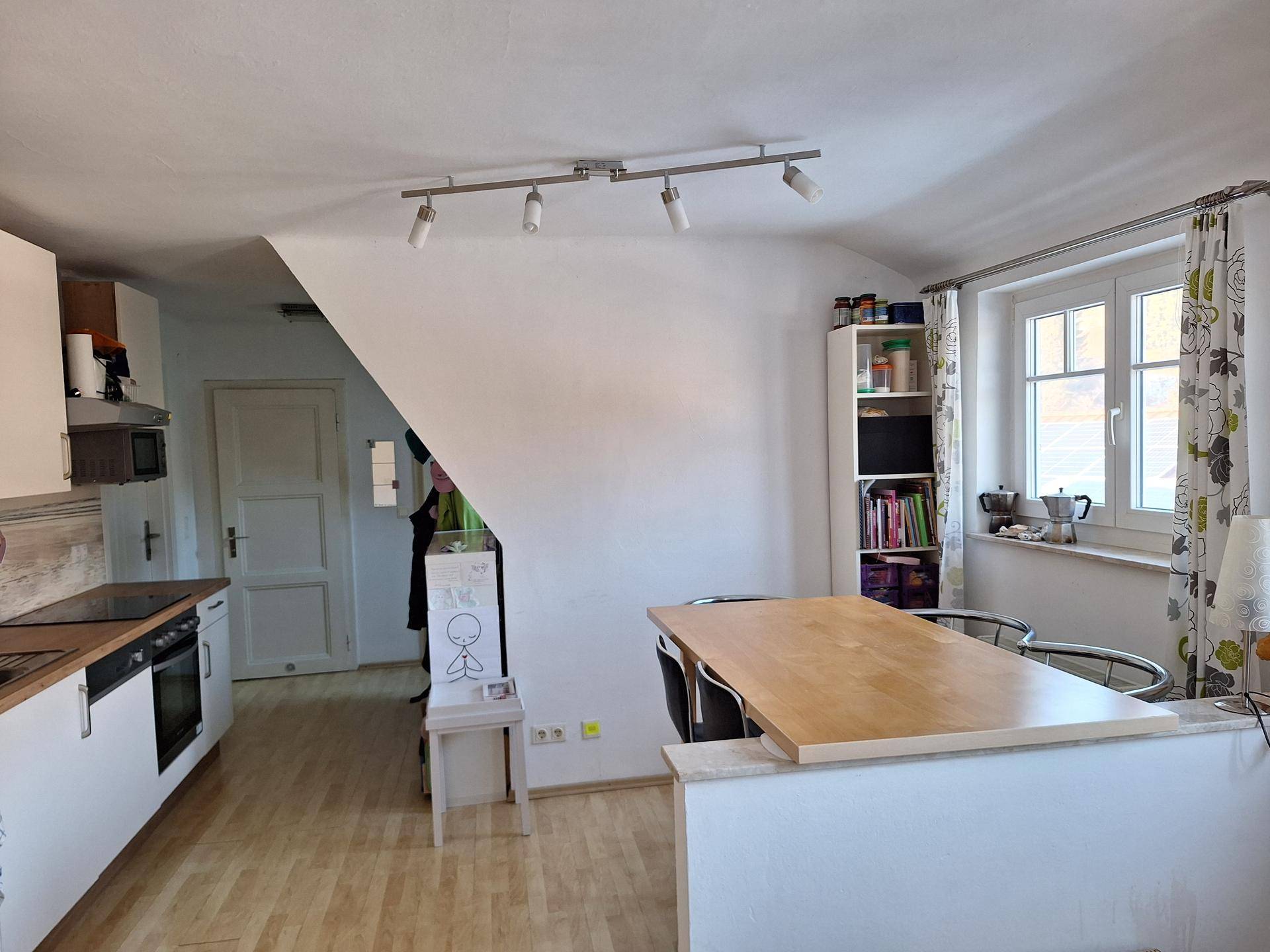 Helle Küche mit Holzarbeitsplatte, weißen Schränken und einem Essbereich am Fenster.