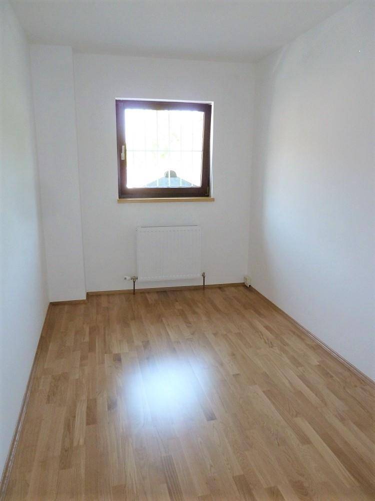 Kleiner, heller Raum mit Holzfußboden und einem Fenster, ideal als Arbeits- oder Kinderzimmer.