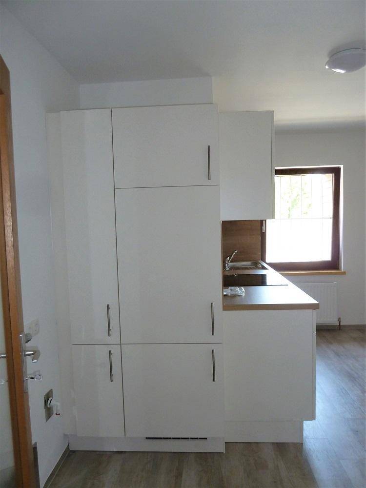 Kompakte Küche mit weißen Schränken, Holz-Arbeitsplatte und Fenster für Tageslicht.