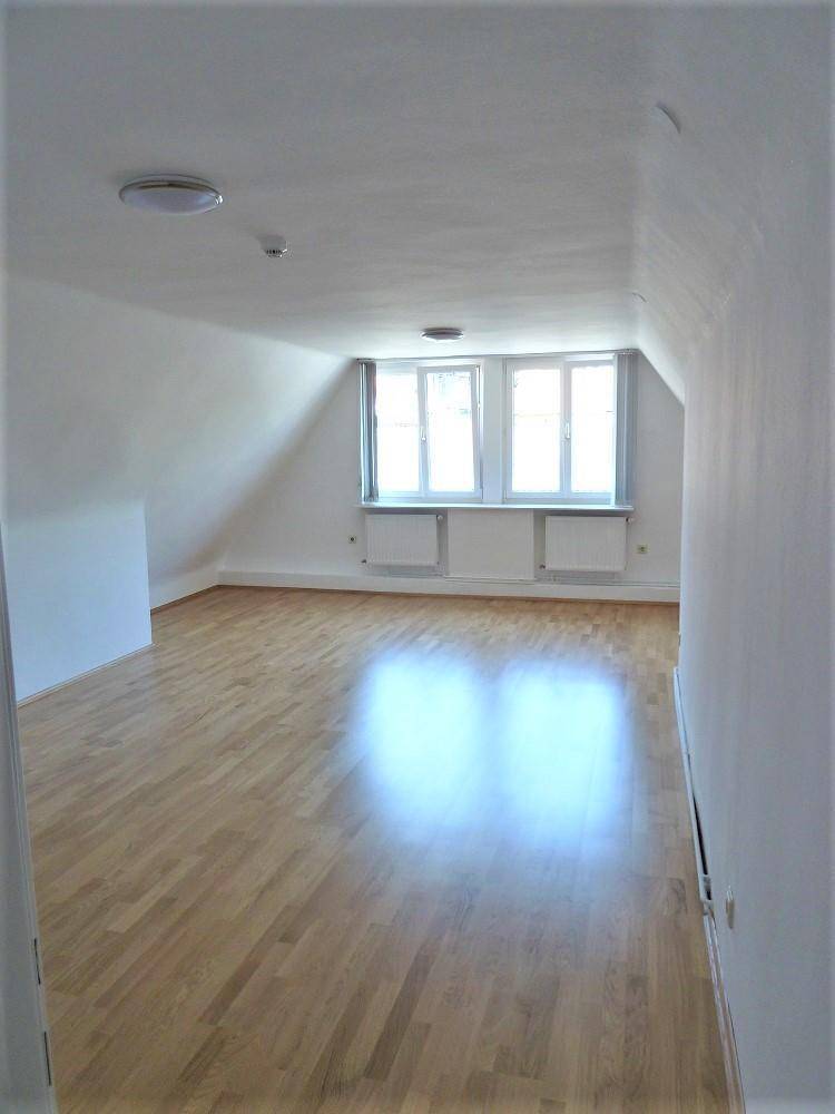 Heller und geräumiger Dachgeschossraum mit Holzfußboden und viel Tageslicht durch die Fenster.