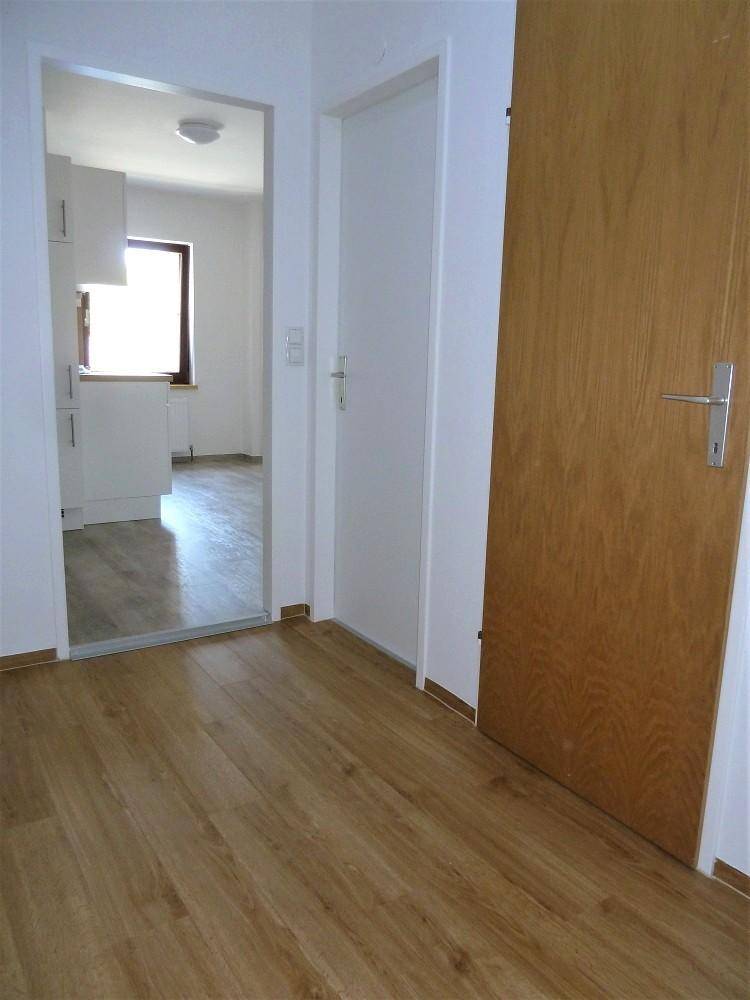 Heller Flur mit Holzfußboden und Blick in die angrenzende Küche.