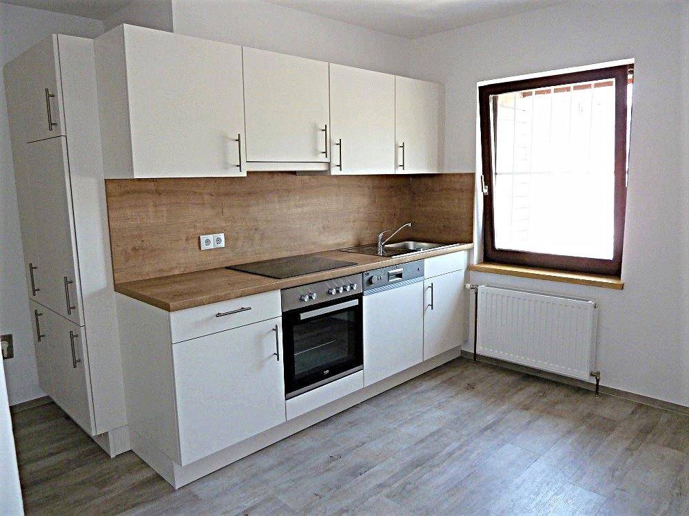 Funktionale Küche mit weißen Schränken, integriertem Backofen und Kochfeld sowie Fenster.
