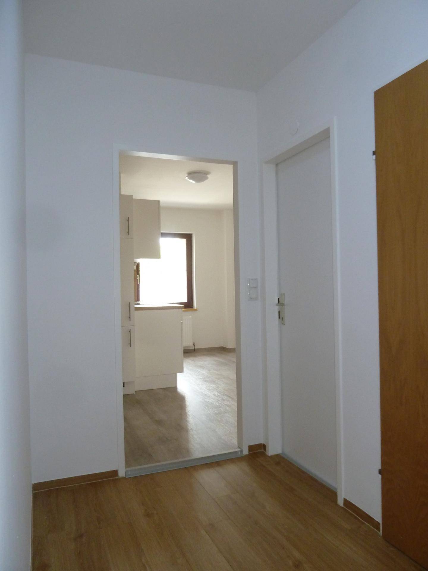 Eingangsbereich mit Holzfußboden und offenem Durchgang zur modernen Küche.