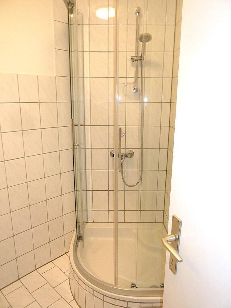 Modernes Badezimmer mit Eckdusche und hellen Fliesen an Wänden und Boden.