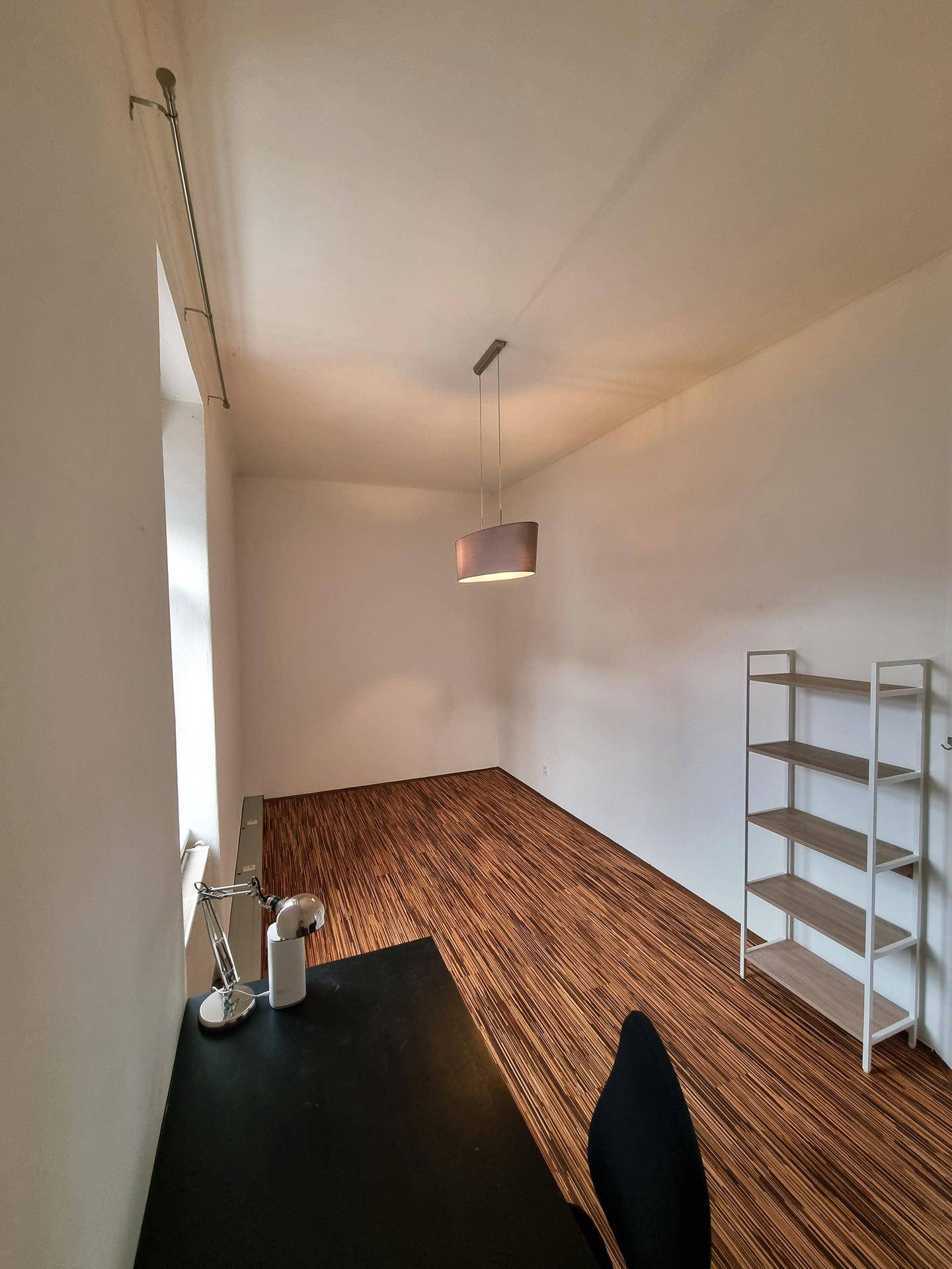 Helles Zimmer mit Holzboden, einem Schreibtisch und einem Regal, ideal als Büro.