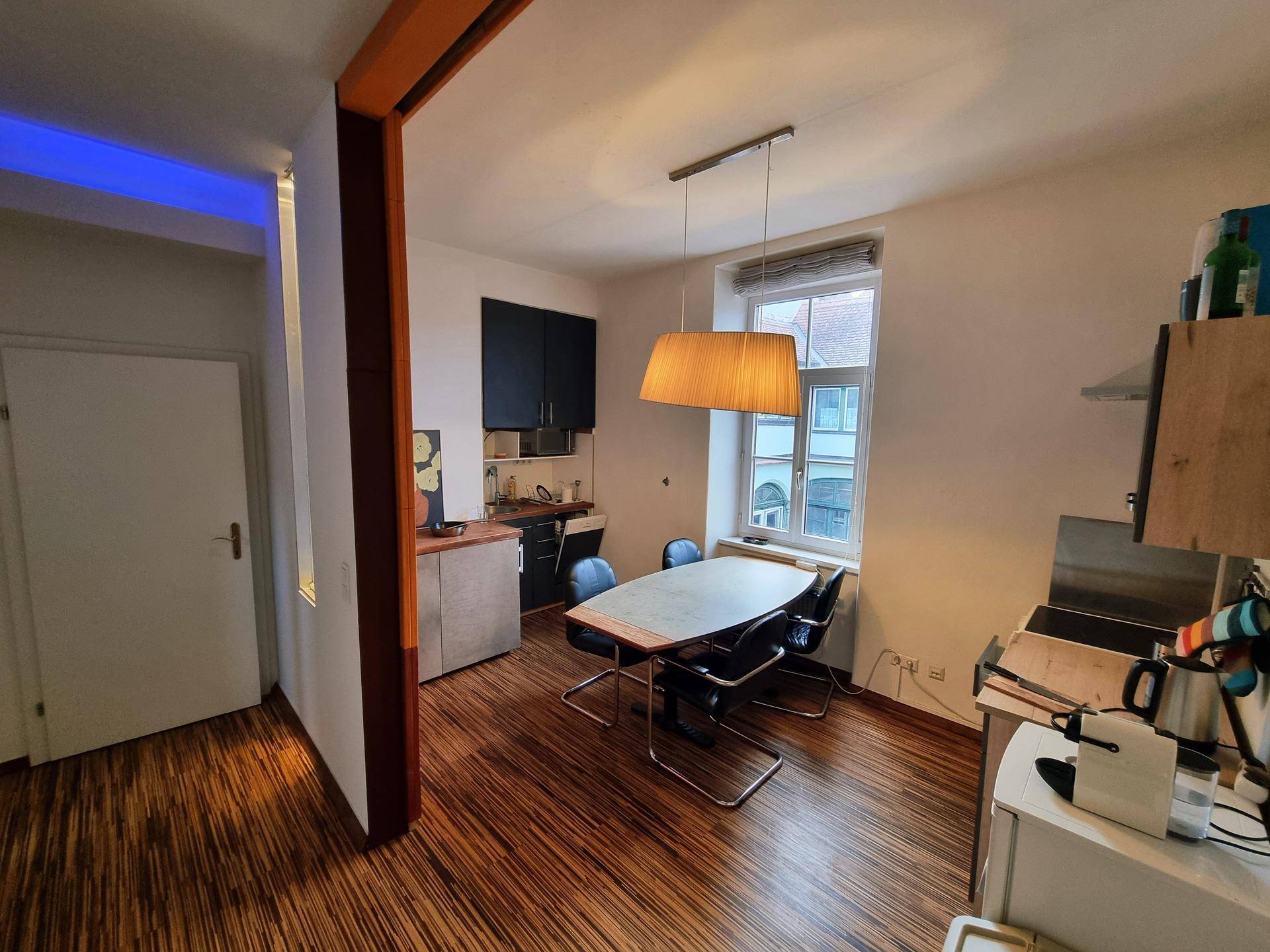 Wohn- und Essbereich mit Holzboden, Fensterblick und integrierter Küchenzeile.