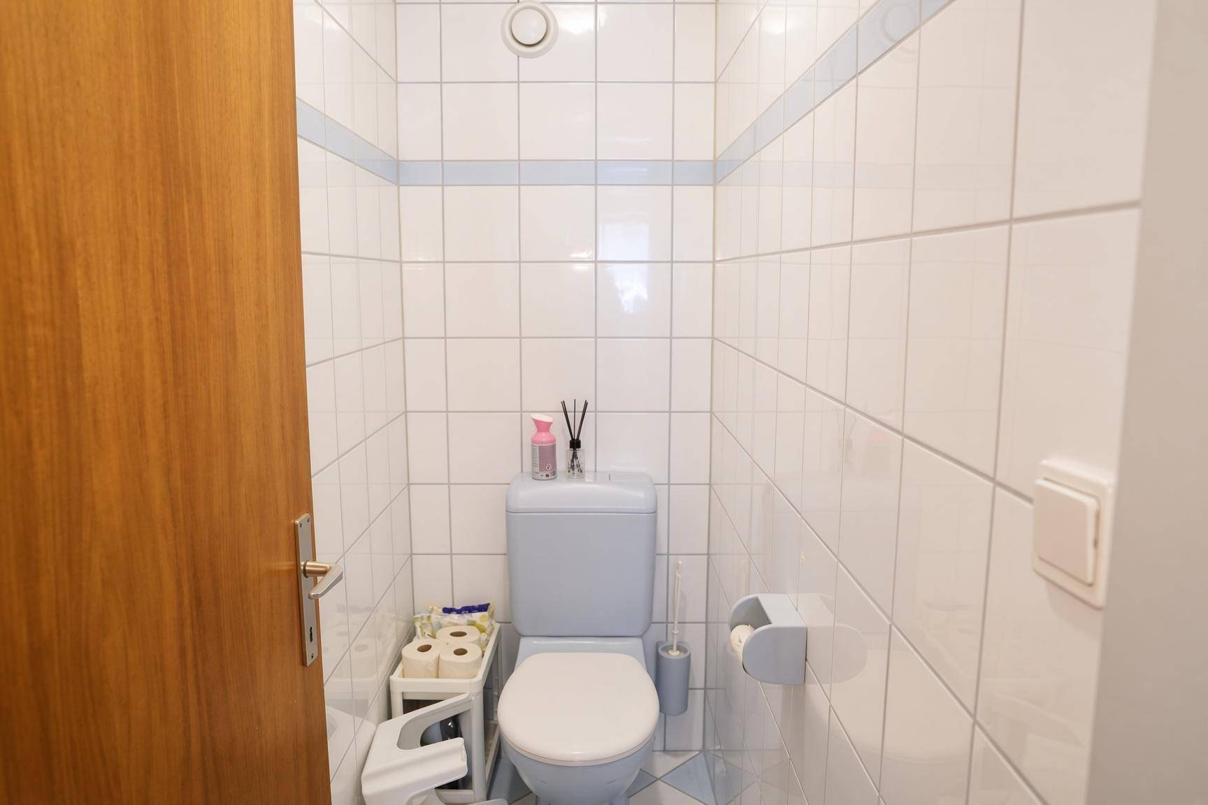 Separates WC mit weißen Fliesen und blauer Zierleiste.