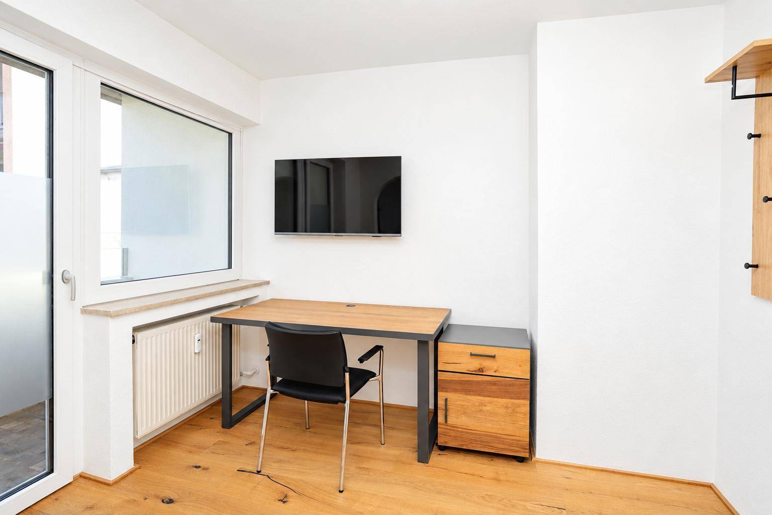 Heller Arbeitsbereich mit Schreibtisch, Wandfernseher und Holzboden in einem modernen Zimmer.