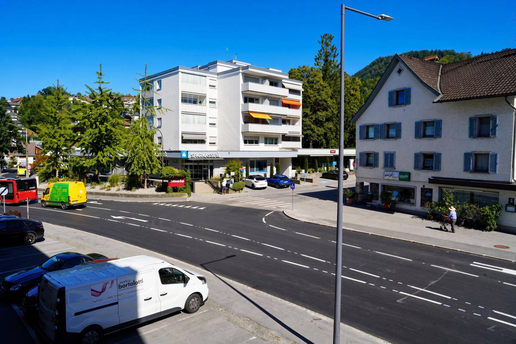 Straßenansicht mit verschiedenen Gebäuden und geparkten Fahrzeugen.