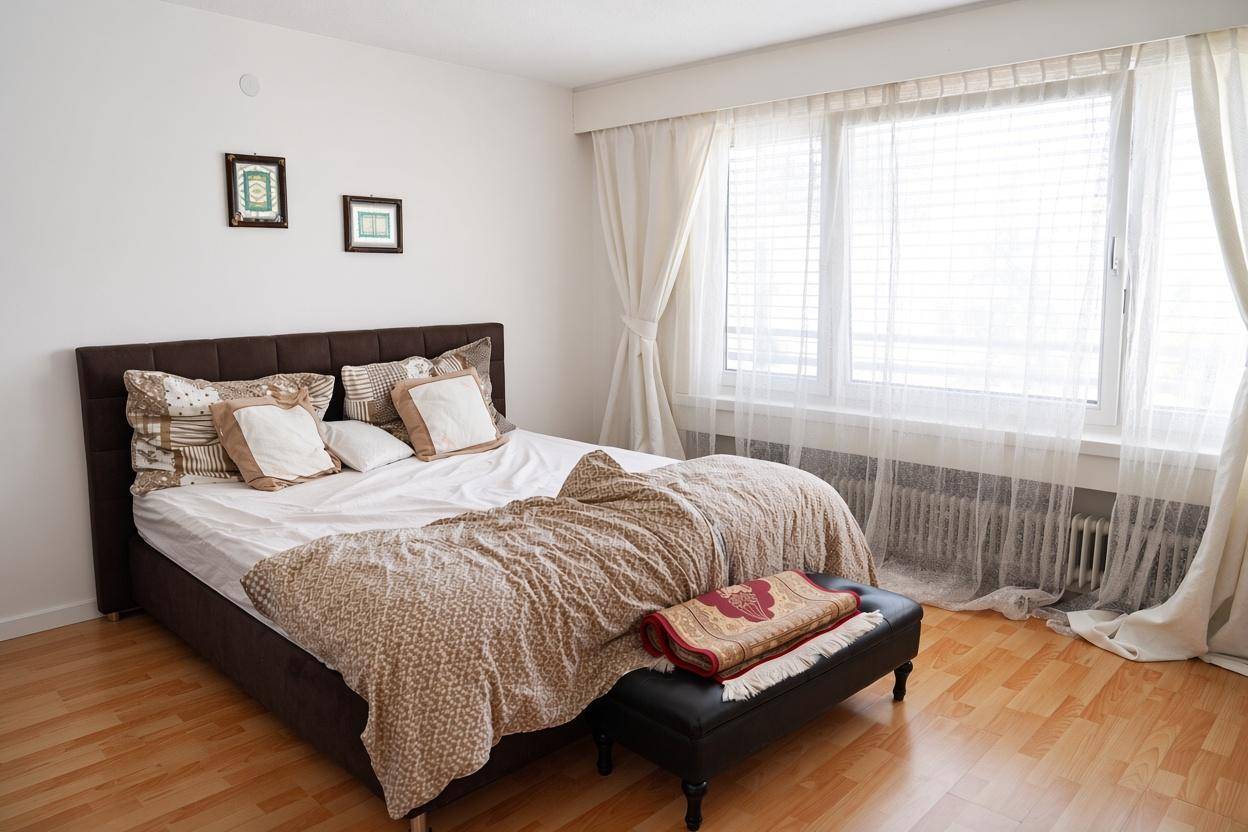 Schlafzimmer mit Doppelbett, Holzboden und großen Fenstern mit Vorhängen.