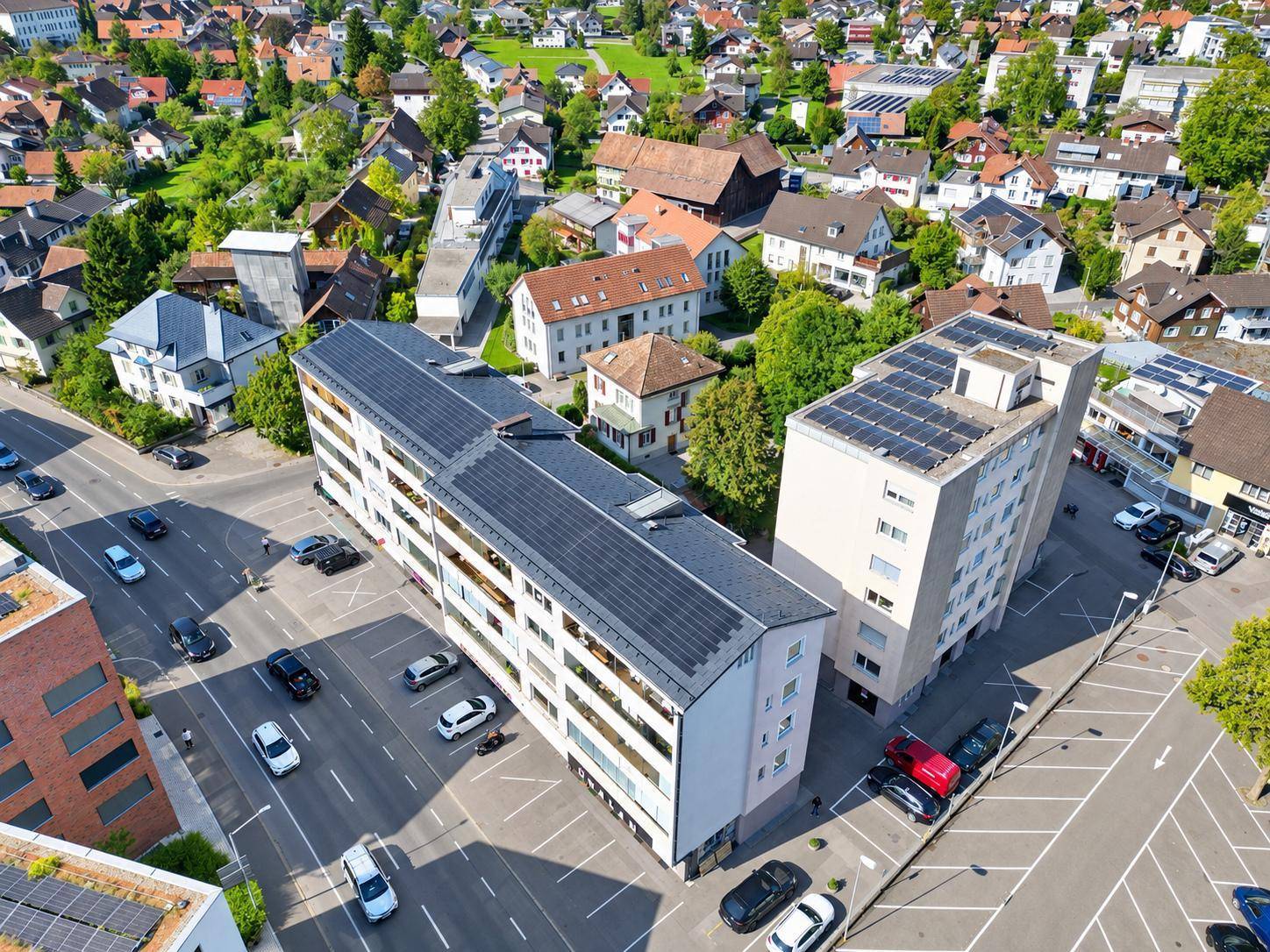 Luftaufnahme eines modernen Wohngebäudes mit Solaranlagen auf dem Dach in einer grünen Umgebung.