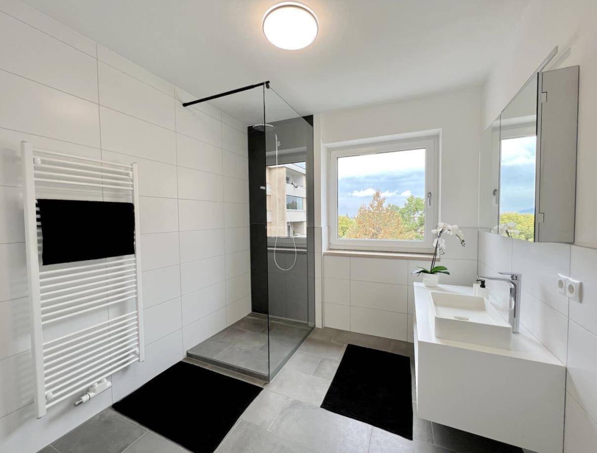 Modernes Badezimmer mit großer begehbarer Dusche, Einzelwaschbecken und Fenster für Tageslicht.
