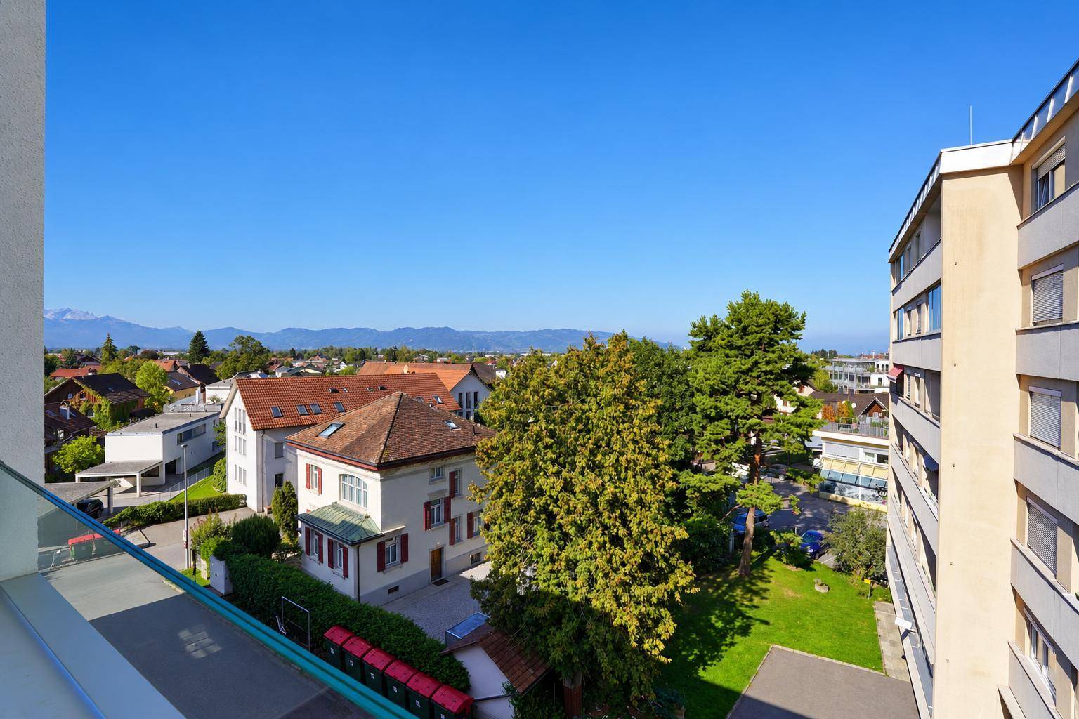Balkon mit Glasbrüstung und weitem Blick über die Stadt und die Berge im Hintergrund.