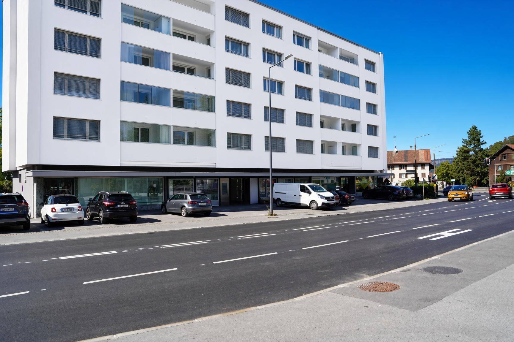 Moderne Wohnanlage mit weißer Fassade und vielen Fenstern an einer Straße gelegen.