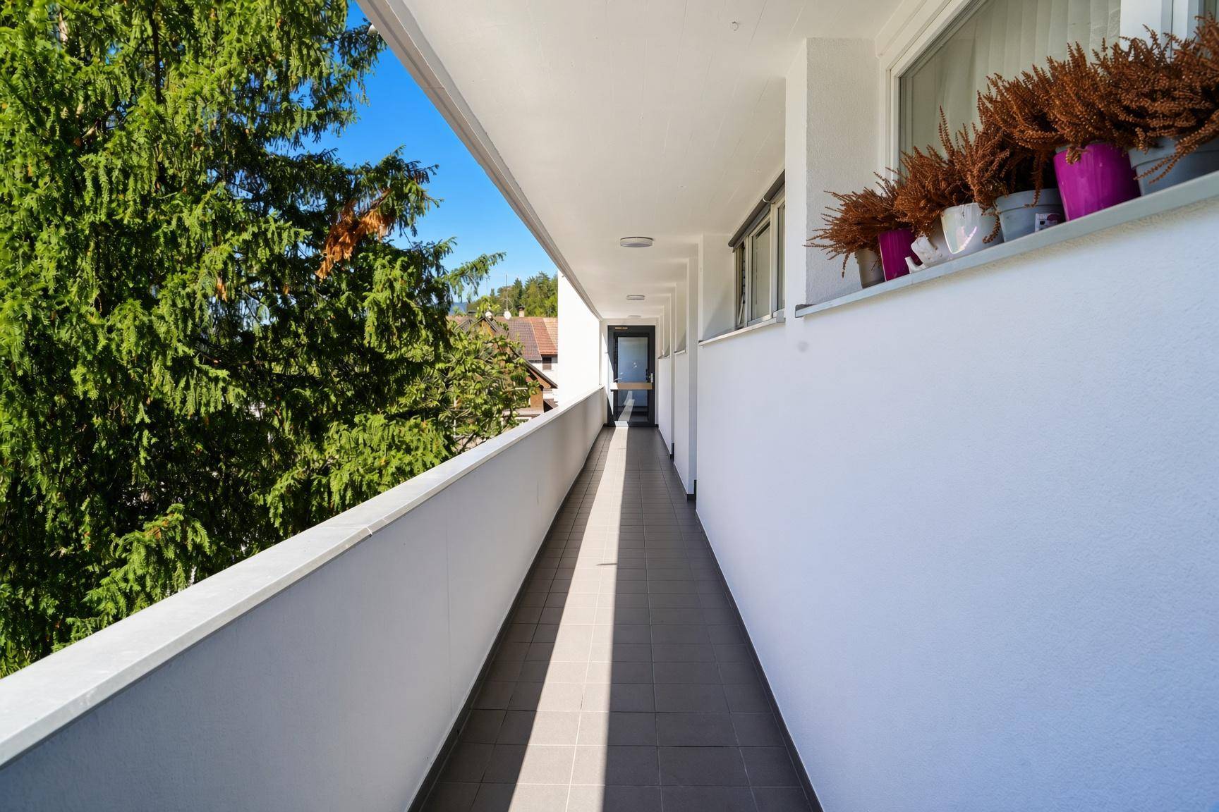 Langer Balkon mit Fliesenboden und Blick ins Grüne.